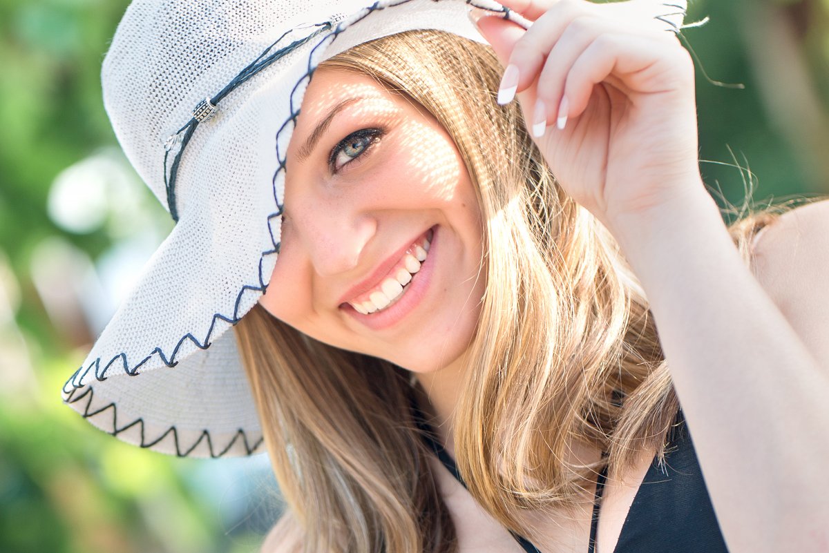 Senior girl poses with hand on hat with only one eye showing.  Photo by Justine, photographer in Bismarck ND