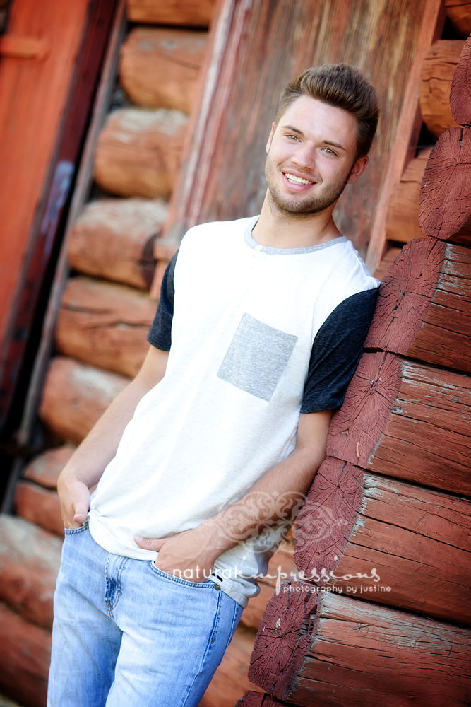 Senior boy posing by log cabin