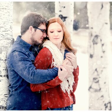 Couple cuddles in winter next to birch trees and snow. Photo by Justine, a wedding photographer in Bismarck ND