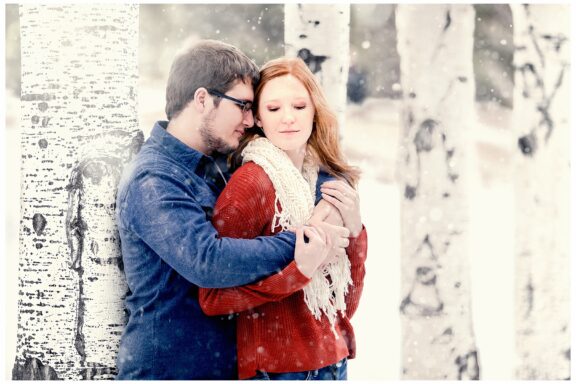 Couple cuddles in winter next to birch trees and snow. Photo by Justine, a wedding photographer in Bismarck ND