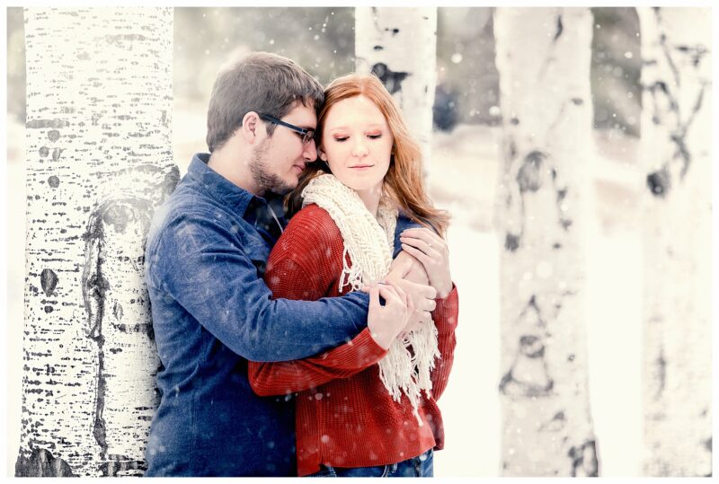 Couple cuddles in winter next to birch trees and snow. Photo by Justine, a wedding photographer in Bismarck ND