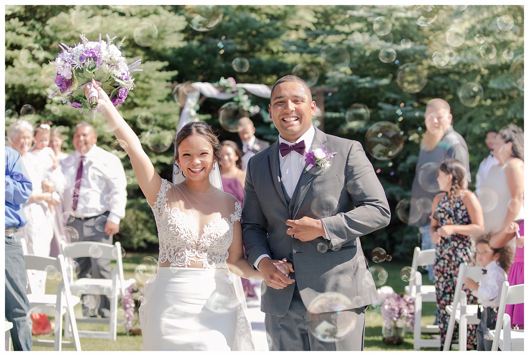 Bride and Groom exit outdoor ceremony, waving purple bouquet and with bubbles.  Photo by photographer in Bismarck ND, Justine