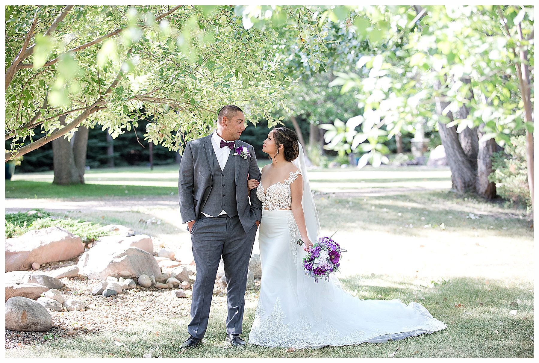 Bride and groom look at each other under trees.  Lavender bouquet and custom gown worn by the bride.  Bismarck wedding photographer, Photography by Justine