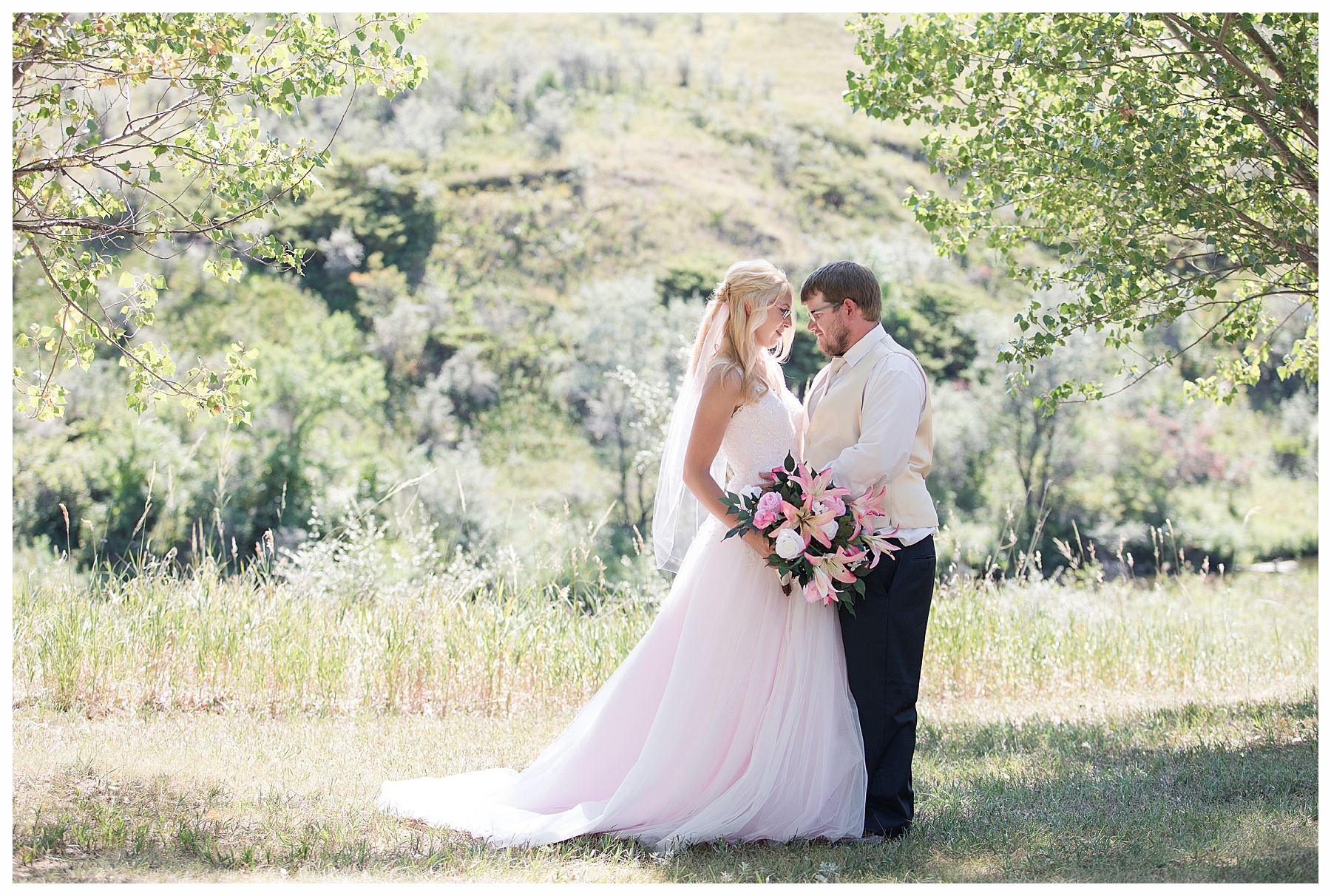 Bride in pink gown and groom in navy look at each other with downstream river behind them.  