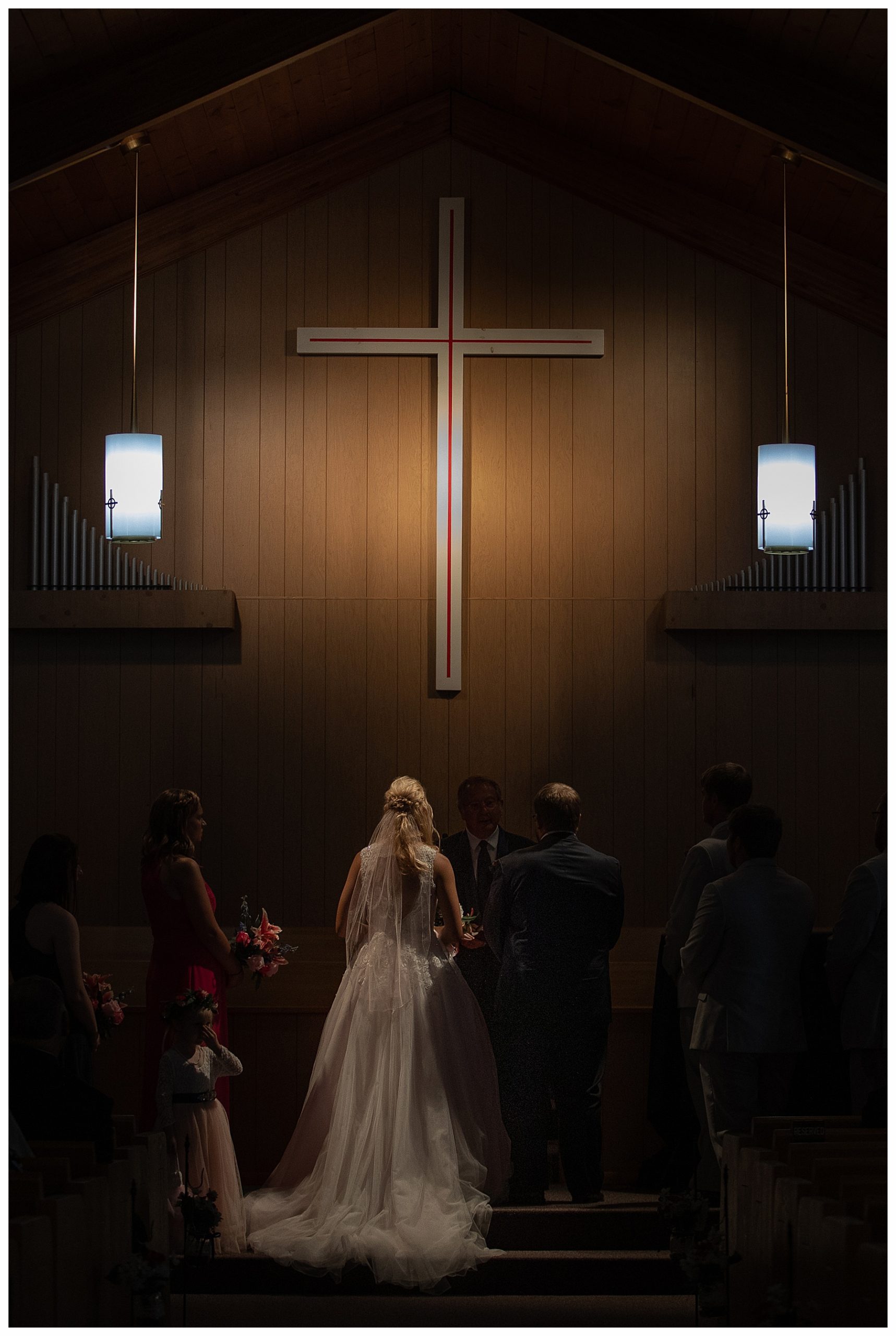 bride and groom in dimly lit classic church.  Back of brides gown under light