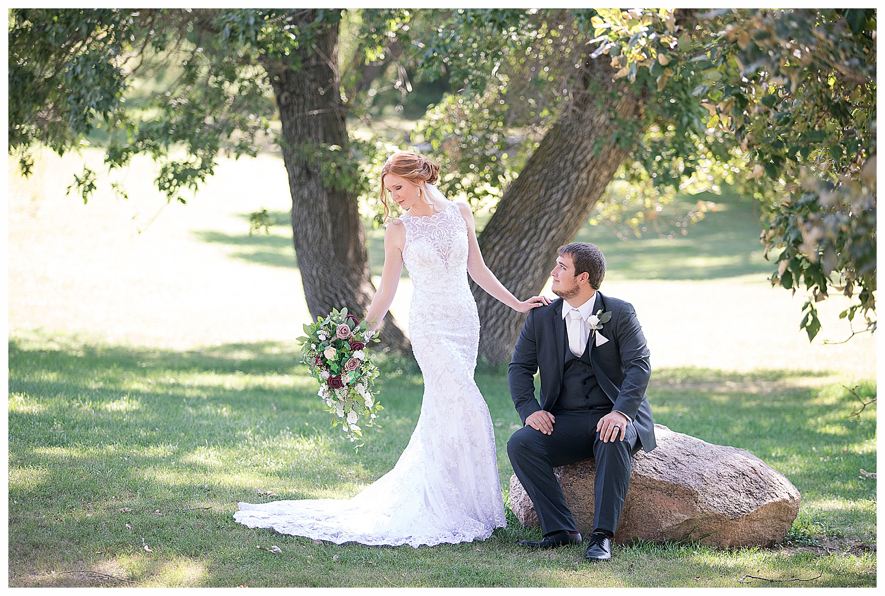 Bride poses in form fitting gown looking at her bouquet while groom looks on at her at Stone Butte Ranch Cabins, Elgin ND