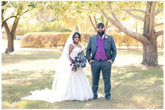 Bride and groom in purple and grey standing together under fall trees