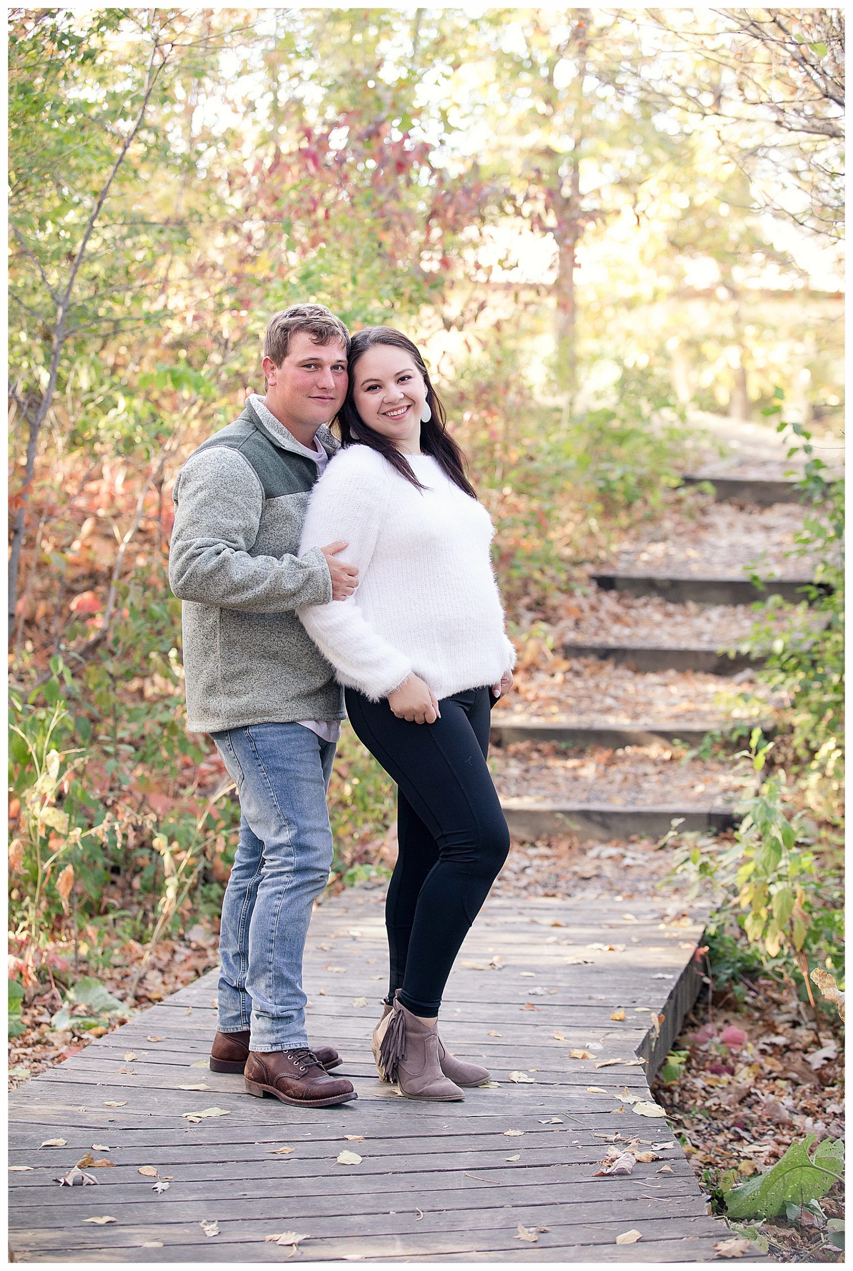 Couple stand together on wooden walk way under fall trees and fall leaves