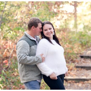 Engaged couple stand on wood steps under fall trees at Sleepy Hollow Park in Bismarck ND