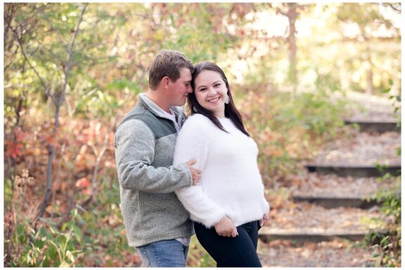 Engaged couple stand on wood steps under fall trees at Sleepy Hollow Park in Bismarck ND