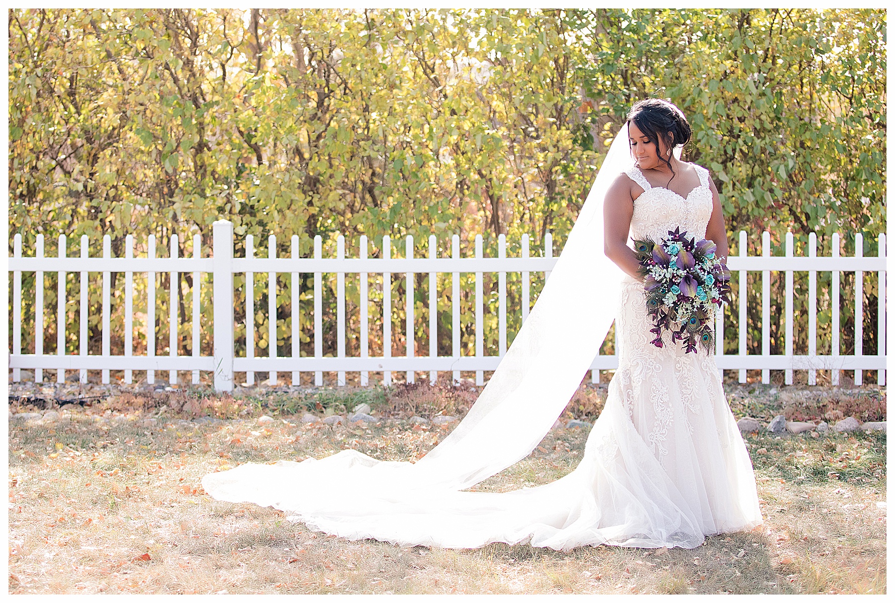 bride with peacock feather bouquet in front of white picket fence