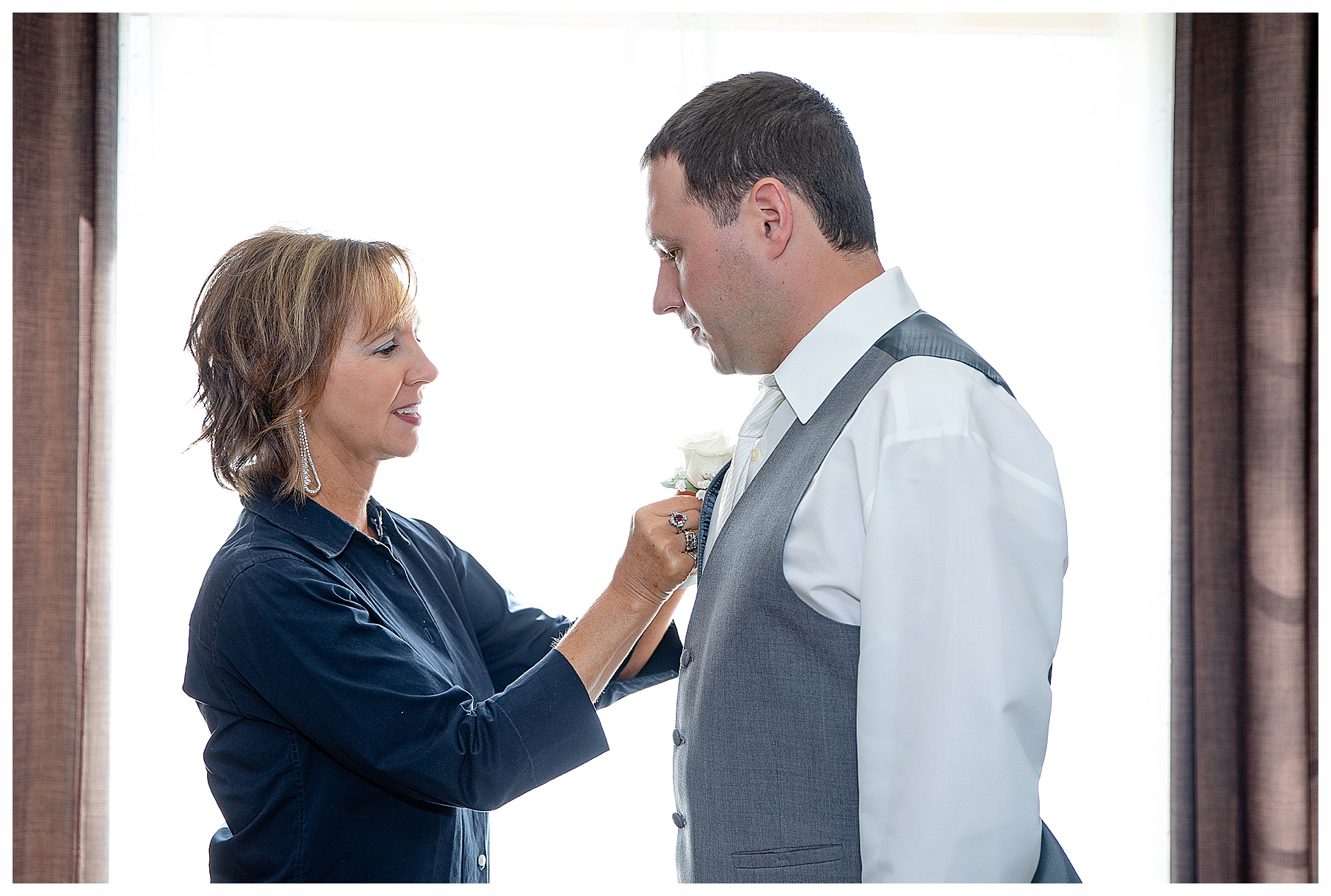 groom in grey tux and mo in navy blue dress helping him pin on flowers