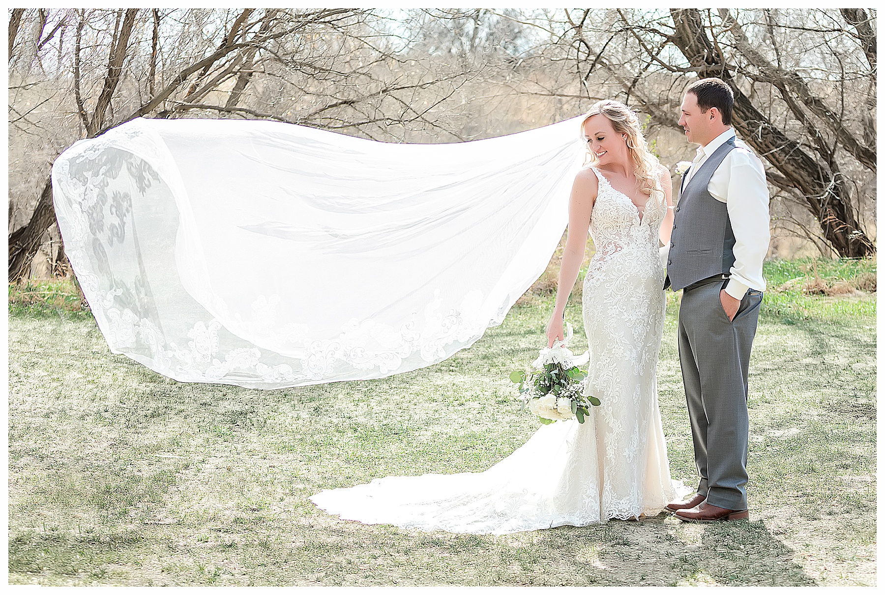 bride and groom watch as cathedral veil blows in the wind. North Dakota May Wedding