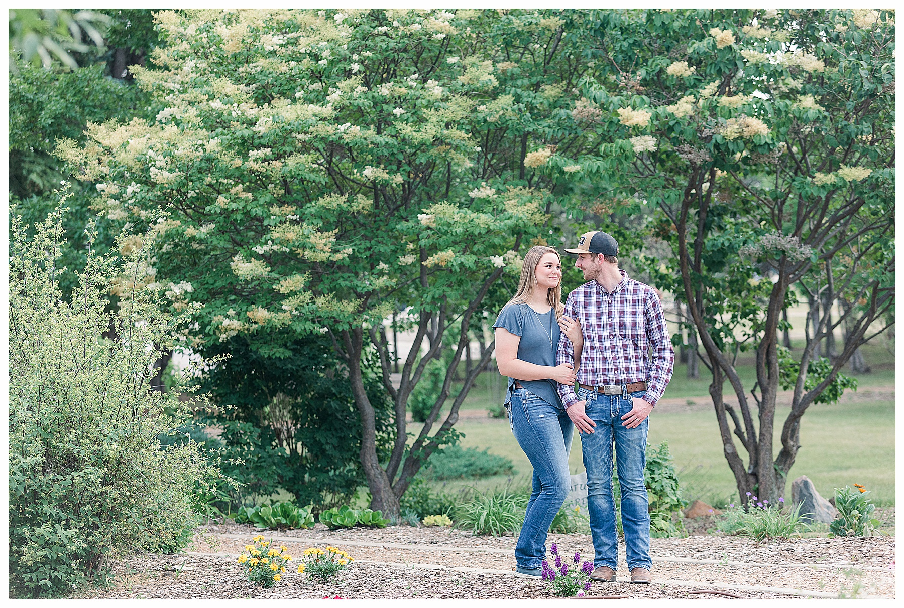 couple stands in front of flowering trees for engagement pictures