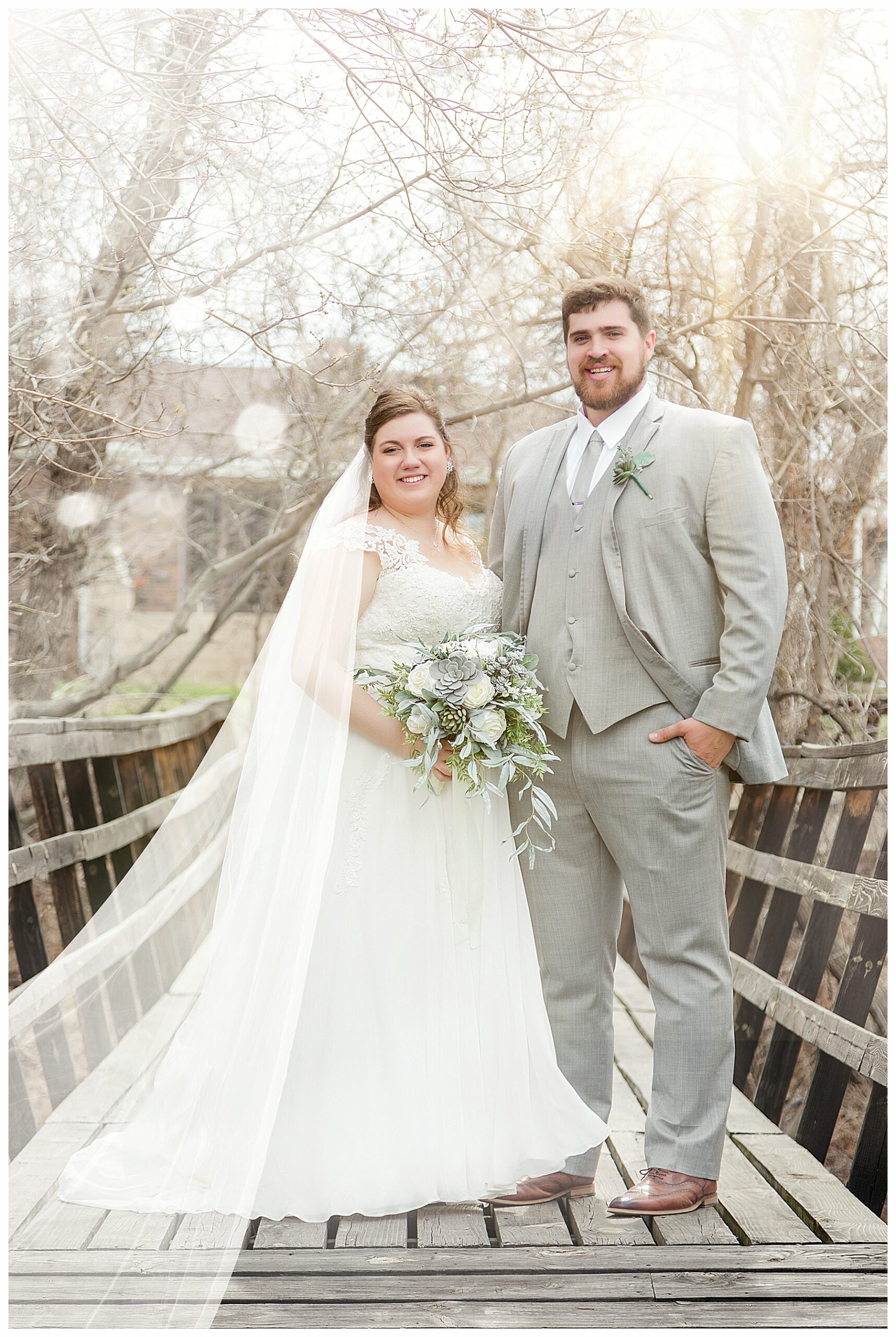 bride in cathedral veil with groom on wood bridge