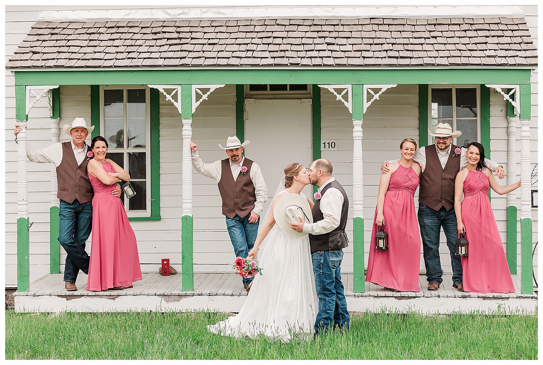 Groom kisses bride while wedding party watches from front porch
